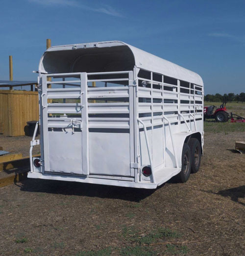 White stock trailer parked in a dirt lot on a farm